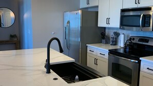 Una cocina moderna con encimera de mármol, electrodomésticos de acero inoxidable e iluminación colgante.
