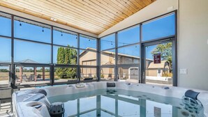 A hot tub area with glass walls and a wooden ceiling, overlooking a residential neighborhood. - Sleeps 30 |  Crew-Friendly | Pool & Hot Tub (Appleton)
