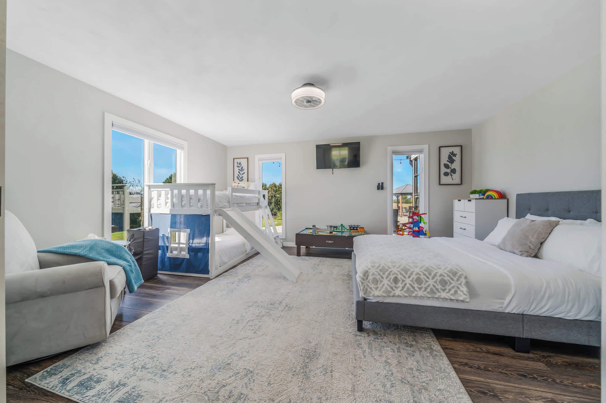 A bedroom with a bed, a desk, a chair, a TV, and a balcony.