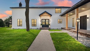 A two-story house with a front porch, a driveway, and a tree in the yard. - Sleeps 30 |  Crew-Friendly | Pool & Hot Tub (Appleton)