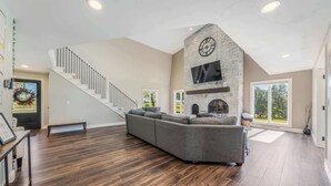 A spacious living area with a large gray sectional sofa, a stone fireplace, and a staircase leading to another level. - Sleeps 30 |  Crew-Friendly | Pool & Hot Tub (Appleton)
