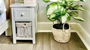 A corner of a room with a white nightstand, a lamp, a clock, a small plant, and a wicker basket. - Welcome home! Your beach cottage awaits! (Fort Lauderdale)