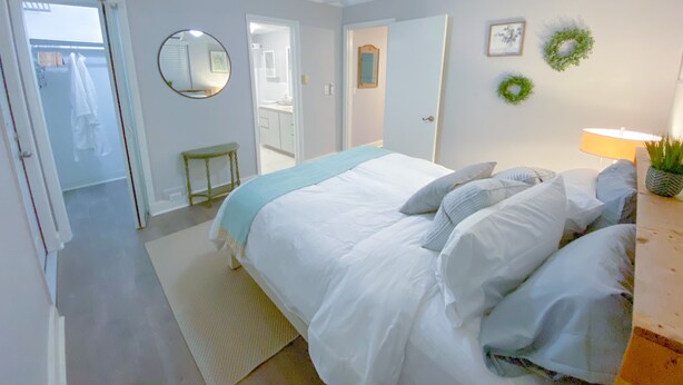 A bedroom with a bed, a ceiling fan, a mirror, and a door leading to a bathroom. - Welcome home! Your beach cottage awaits! (Fort Lauderdale)