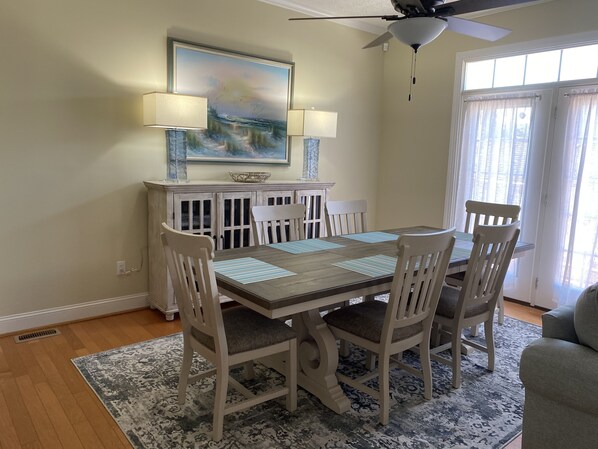 A dining area with a wooden table, white chairs, a patterned rug, and a painting above the table. - Cozy home within walking distance to the beach. Golf cart available for x-fee (Surfside Beach)
