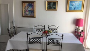 Un comedor con una mesa lista para cuatro personas, rodeada de sillas, y tres obras de arte enmarcadas en la pared.