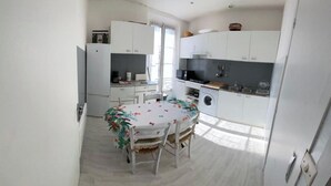 Una cocina compacta con armarios blancos, una mesa de comedor con mantel floral y una lavadora.