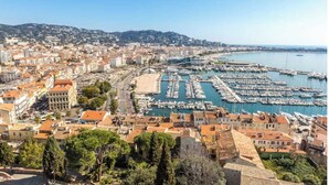 Un paisaje urbano costero con un puerto deportivo lleno de barcos, rodeado de edificios residenciales con tejados de tejas rojas.