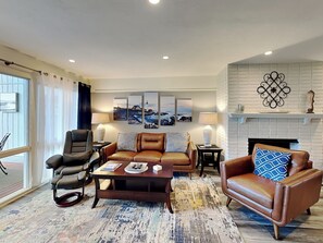 A living room with a leather sofa, a leather armchair, a coffee table, and a fireplace with a white brick wall and decorative items. - Deer Run 9767 by Distinctive Beach Rentals (Ponte Vedra Beach)