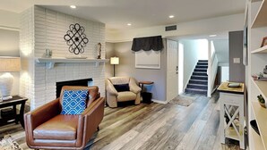 Ein Wohnzimmer mit Kamin, einem Ledersessel, einer Couch und einer Treppe, die in eine weitere Ebene führt.