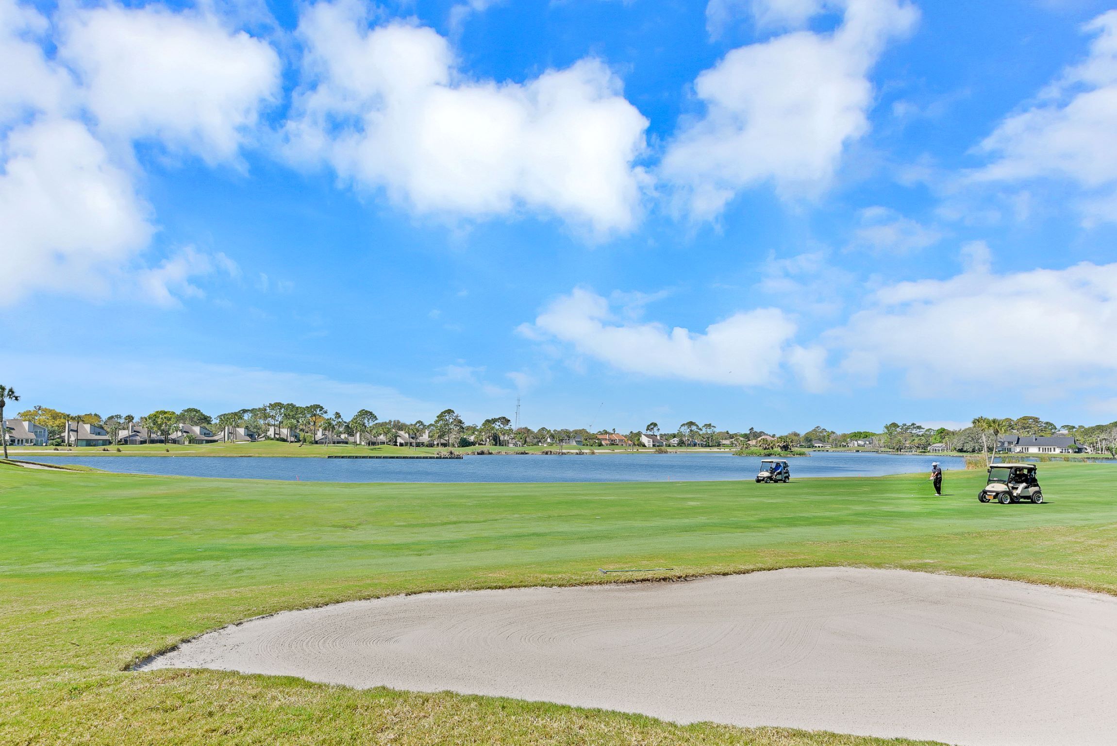 A golf course with a lake, sand bunkers, and a clear blue sky.