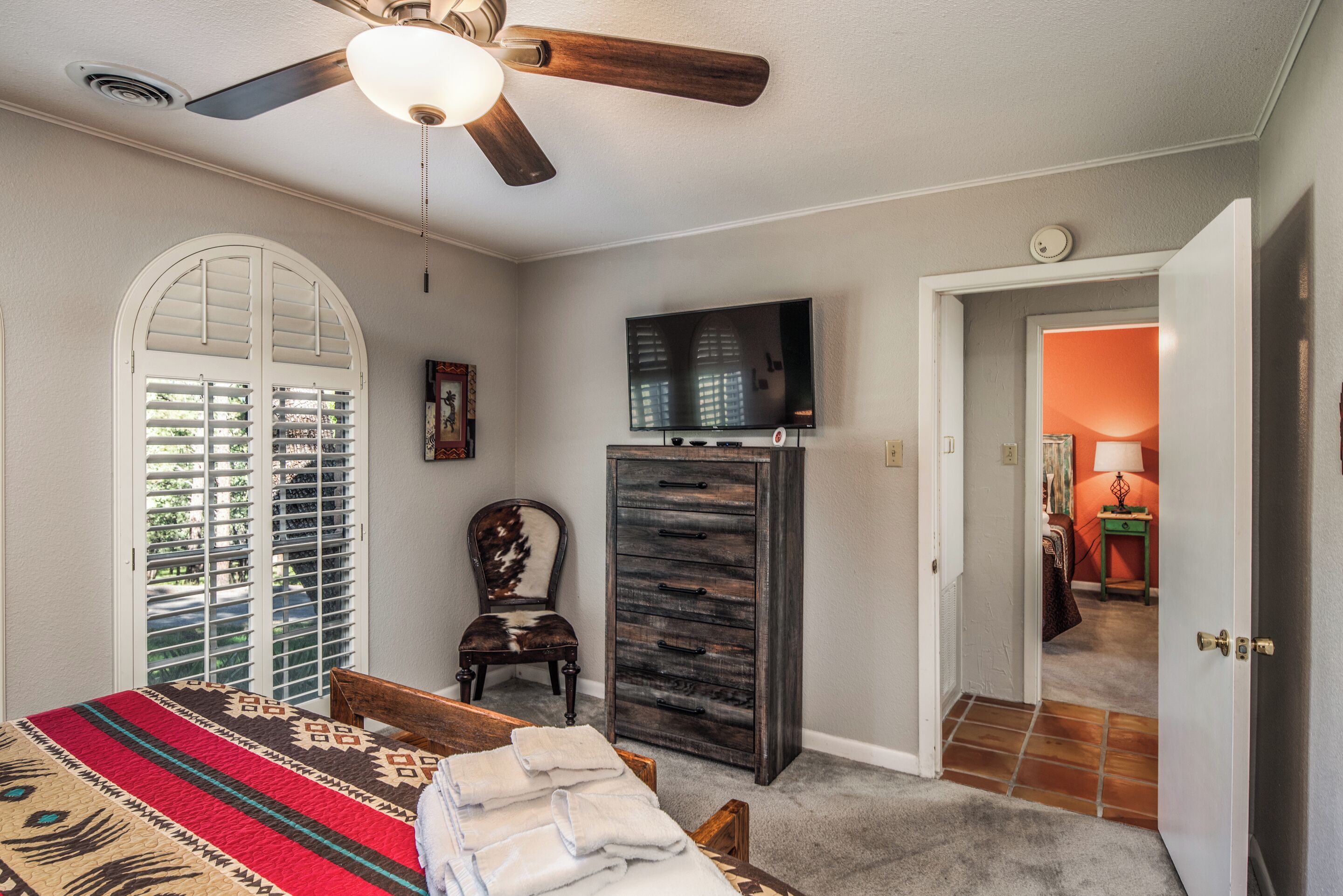 A bedroom with a bed, a dresser, a television, and a ceiling fan.