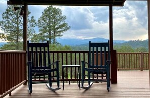 A wooden deck with two rocking chairs and a small table, overlooking a mountainous landscape. - Painted Horse Retreat by Ruidoso Vacation Rentals (Ruidoso)