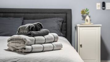 A neatly made bed with folded towels and a bedside table with a vase and a plant.