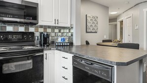 A modern kitchen with stainless steel appliances, white cabinetry, and a large island. - Spacious 3-Bed Downtown, AC, Heated Underground Prkg, Near Saddledome & Stampede (Calgary)