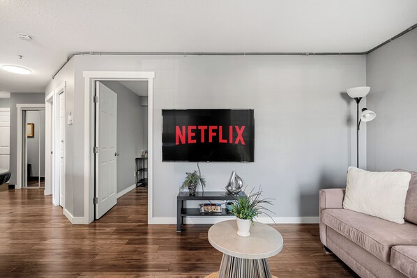 A modern living room with a flat-screen TV mounted on the wall, a round coffee table, a sofa, and a potted plant. - Stylish 3 Beds, Underground Parking, A/C, Stampede & Saddledome (Calgary)