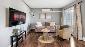 A modern living room with a flat-screen TV, a sofa, a chair, and a coffee table. - Spacious 3-Bed Downtown, AC, Heated Underground Prkg, Near Saddledome & Stampede (Calgary)