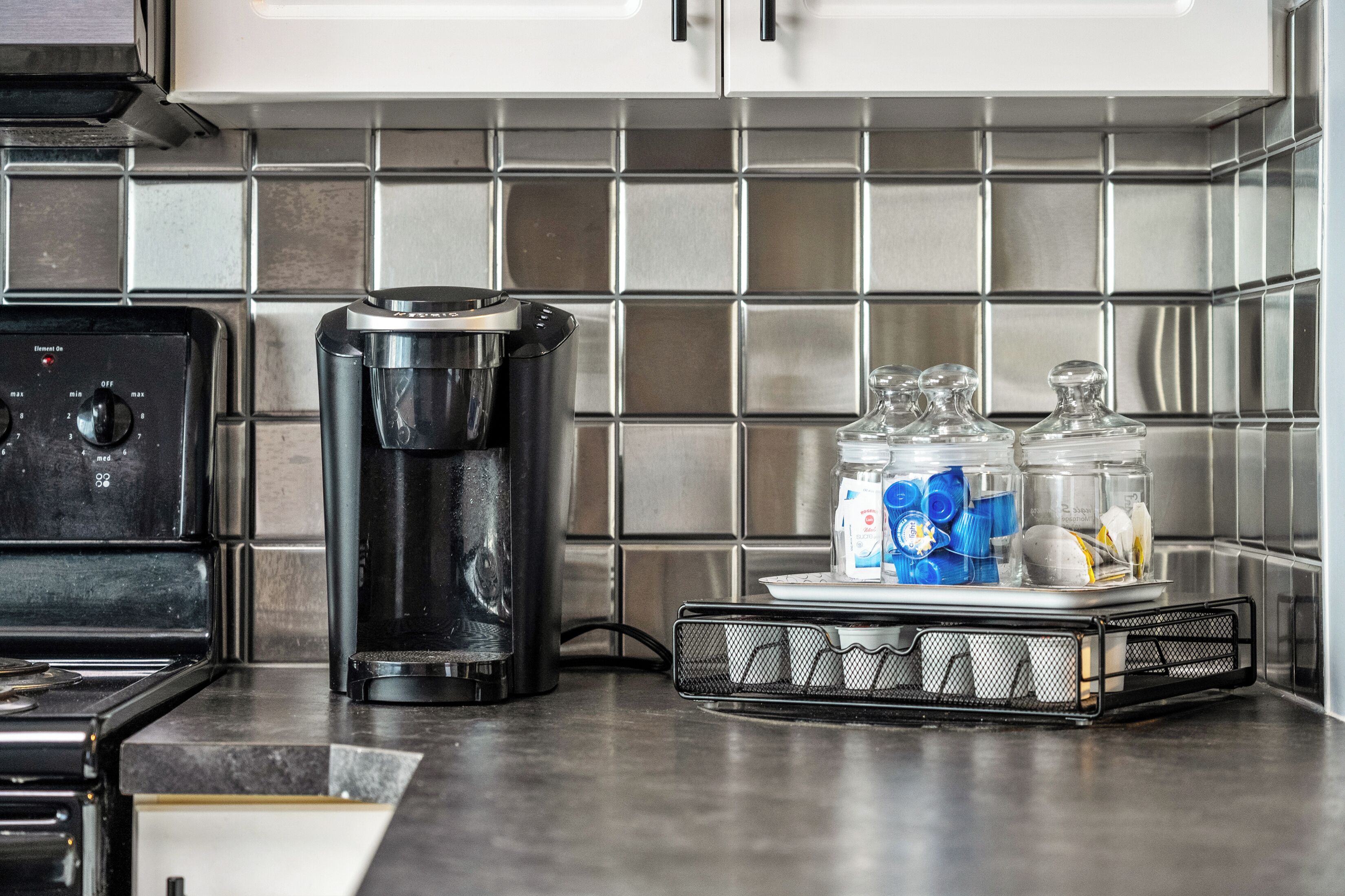A kitchen with a coffee maker, a scale, and glass containers on the counter.