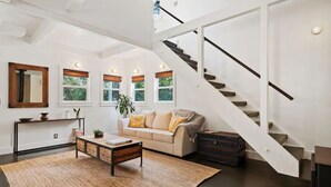 Un salón comedor espacioso con techo alto, una escalera y un ventanal con vistas al verdor.