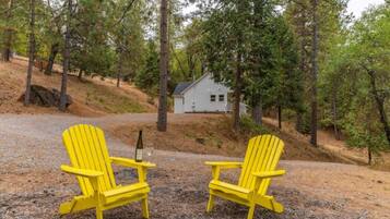 Twee gele Adirondack stoelen staan op een grindpad, met op de achtergrond een huis omringd door bomen.