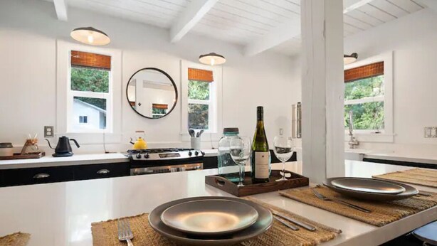 Una cocina moderna con encimeras blancas, una isla central y amplias ventanas.