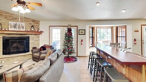 Un salon moderne avec une cheminée, un grand canapé, un coin repas avec des tabourets de bar et un sapin de Noël.