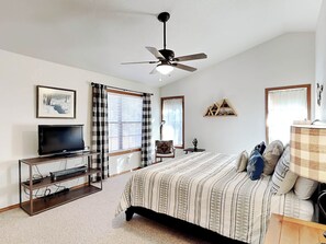 Relax in a serene bedroom with a large bed, ceiling fan, flat-screen TV, and a window with blinds.
