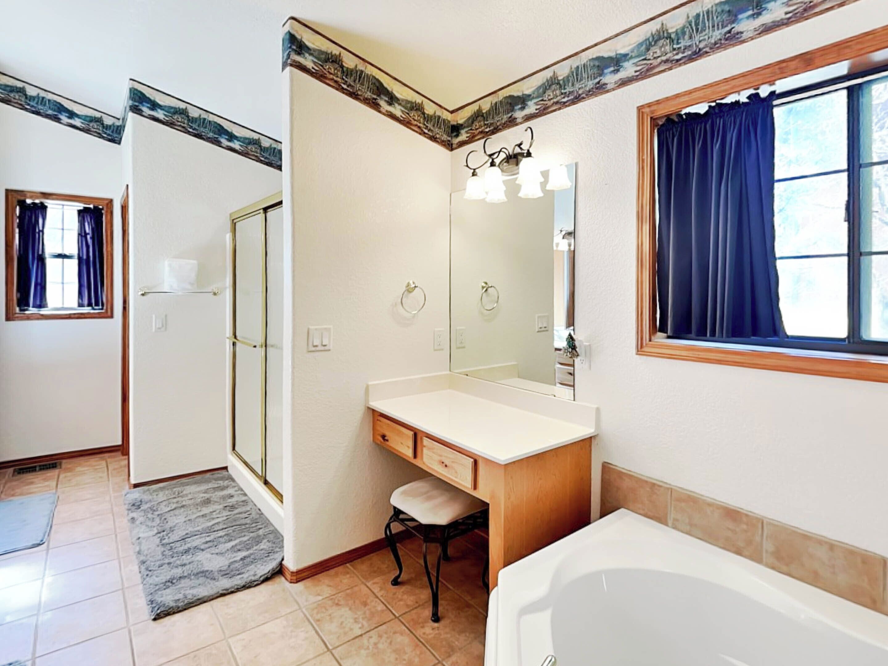 A bathroom with a bathtub, a vanity with a mirror, a shower, and a window with curtains.