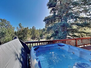 Relax in a hot tub on a raised deck overlooking a forest.