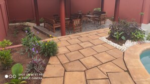 A patio area with a thatched roof, wooden furniture, and a swimming pool.