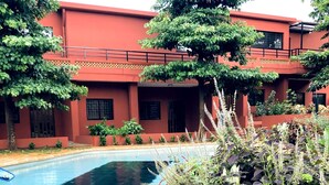 A swimming pool surrounded by a garden with various plants and a building with a red facade in the background.