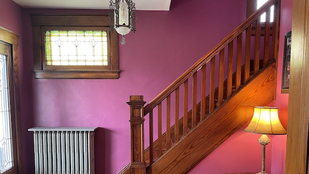 A staircase with wooden railings, a radiator, a window with stained glass, and a table with a lamp and a book. - Vintage Oakley Home (Cincinnati)
