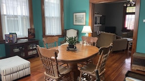 A dining area with a wooden table and chairs, a sofa, and a television in the background. - Vintage Oakley Home (Cincinnati)