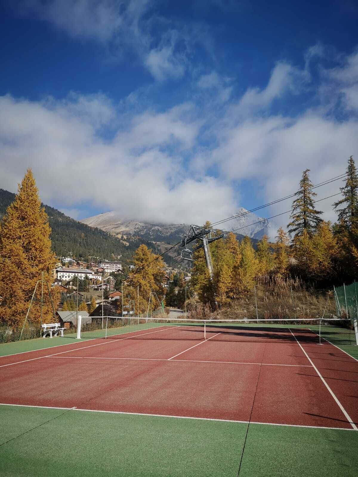Ein Tennisplatz mit Netz, umgeben von Bäumen und Bergen im Hintergrund.