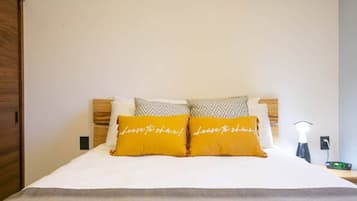 A neatly made bed with two pillows, a bedside table with a lamp, and a wall-mounted air conditioner.