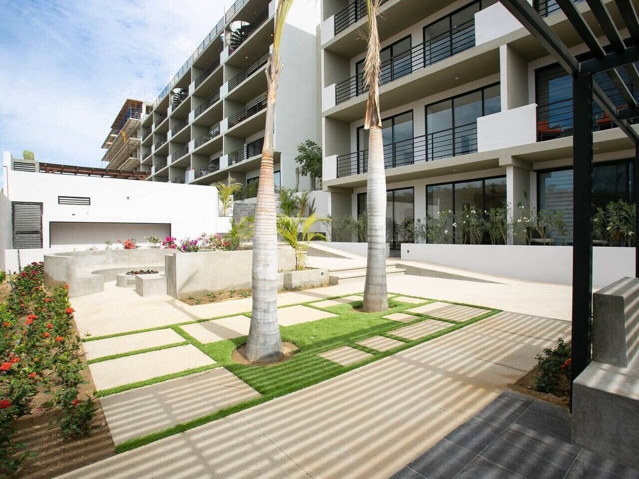 Un bâtiment moderne doté de nombreux balcons, une cour aménagée avec des palmiers et un ciel dégagé.