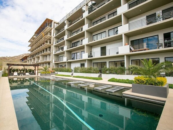 A multi-story hotel with a swimming pool, outdoor seating, and balconies.