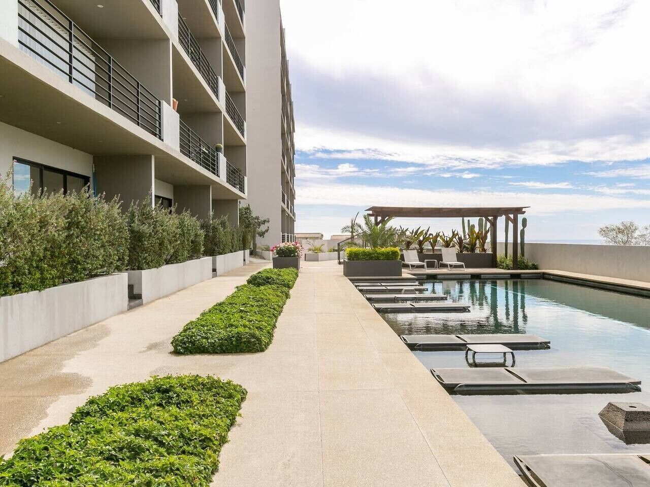 Uma área de piscina moderna de hotel com céu claro, um caminho que leva à piscina e cadeiras de descanso.