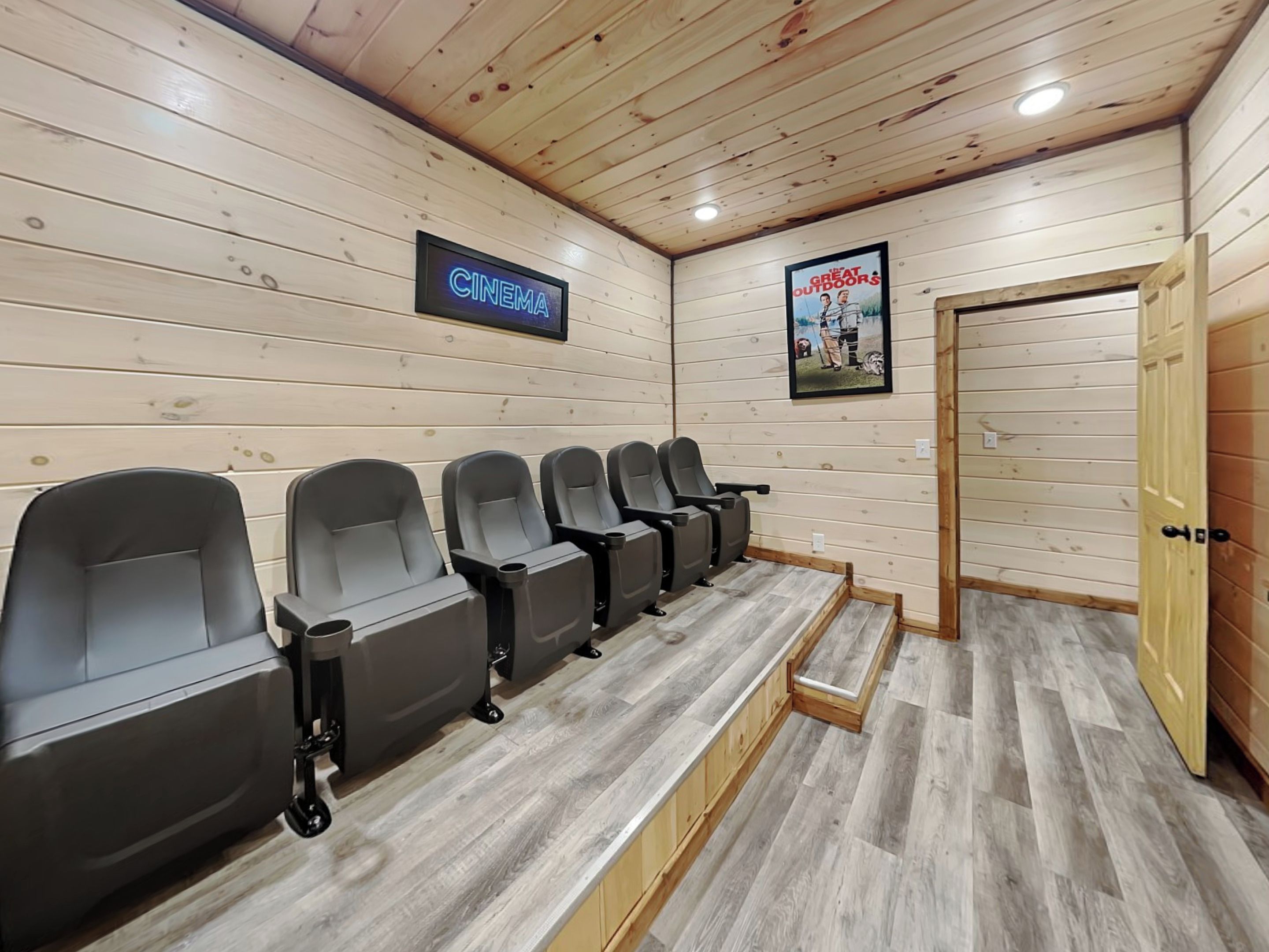 A cinema room with wooden walls, a sign reading "CINEMA," and a poster of "Great Outdoors."