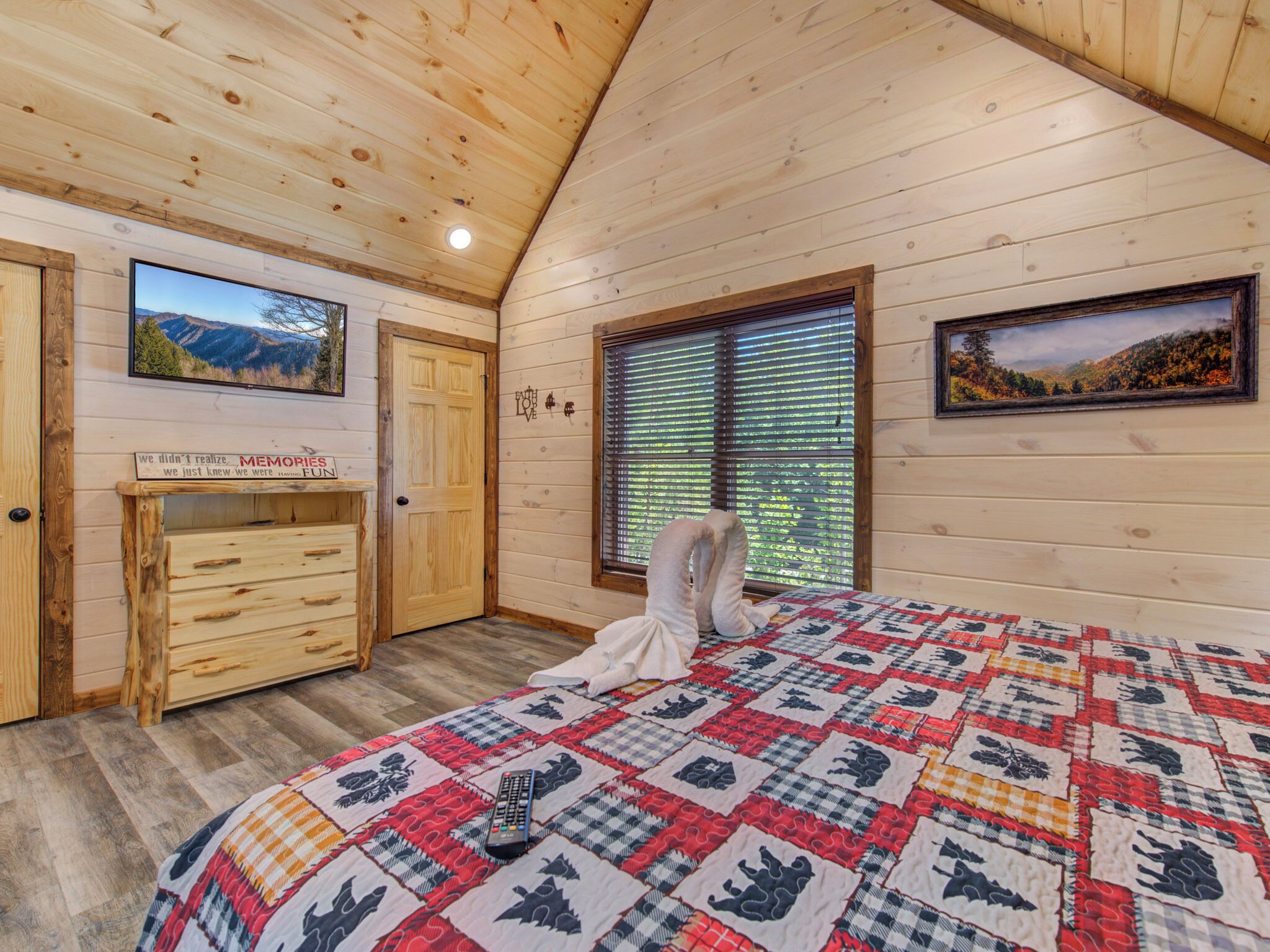 Ein gemütliches Schlafzimmer mit Holzbalkendecke, einer gesteppten Bettdecke, einem Schminktisch und zwei gerahmten Bildern an den Wänden.