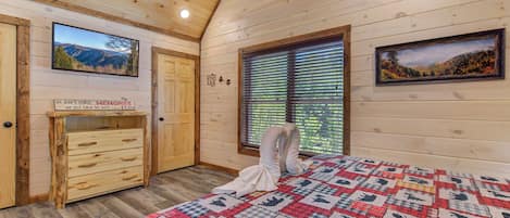 Ein gemütliches Schlafzimmer mit Holzbalkendecke, einer gesteppten Bettdecke, einem Schminktisch und zwei gerahmten Bildern an den Wänden.