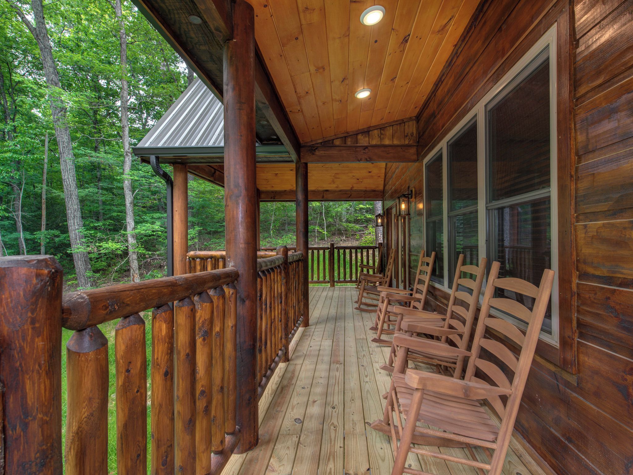 A wooden deck with a railing, wooden chairs, and a view of the forest.