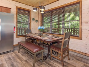 A wooden cabin interior with a dining table, benches, and a refrigerator.