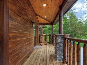 Una cabaña de madera con un revestimiento de piedra, una terraza de madera y vistas al bosque circundante.