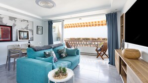 A modern living room with a teal sofa, a dining table, and a balcony with a view. - Apartment Royal Sunset Loggia (Palm-Mar)