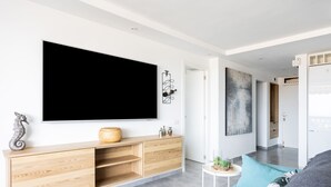 A modern living room with a large flat-screen TV, wooden entertainment unit, teal sofa, and a small side table with decorative items. - Apartment Royal Sunset Loggia (Palm-Mar)