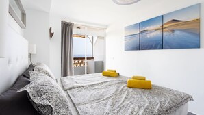 A hotel room with a bed, a window with curtains, a balcony, and a wall-mounted artwork. - Apartment Royal Sunset Loggia (Palm-Mar)