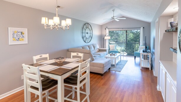 Un comedor con una mesa de madera y sillas blancas, un sofá y un ventilador de techo.