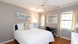 Un dormitorio con cama, ventilador de techo, obra de arte y un escritorio con silla.