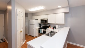 Una cocina moderna con armarios blancos, un lavamanos de acero inoxidable, un refrigerador, un microondas y un horno.