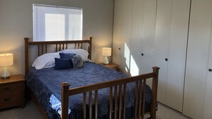 A bedroom with a wooden bed, two bedside tables with lamps, a window with blinds, and a wardrobe. - Morning Coffee with the quail.  Great views, excellent trails, and work friendly (Grand Junction)